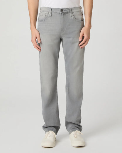 A person stands facing forward, wearing Paige Grey Wainwright Normandie Regular Fit Jeans with a white tucked-in shirt and white sneakers. Only the lower body is shown, hands at the sides, against a plain light grey background. , available at Richard Gelding Mayfair