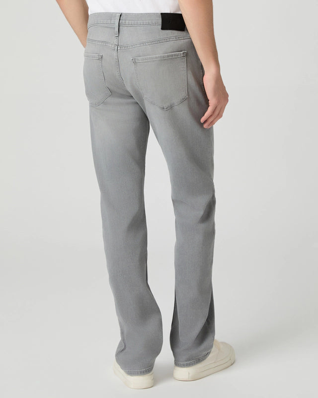 A person wears Paige Grey Wainwright Normandie Regular Fit Jeans with two back pockets, paired with a white shirt and white sneakers. Only the lower half is shown against a plain, light background. , available at Richard Gelding Mayfair