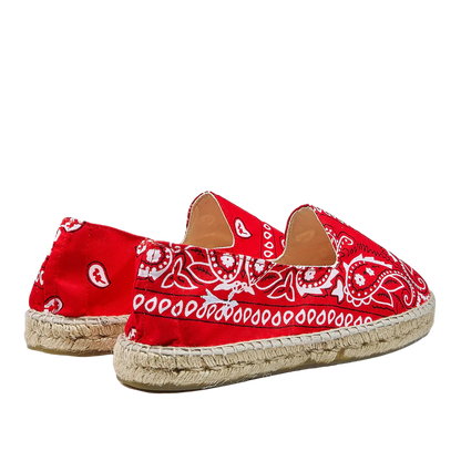 A pair of Red Cotton Bandana Print Manebi espadrille shoes on a striped background.