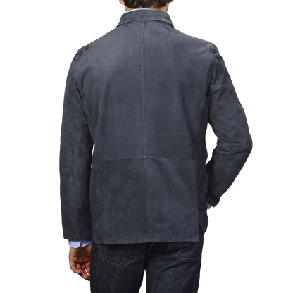 Back view of a person wearing the Denim Blue Suede Unlined Jacket by Manto and blue jeans against a plain background.