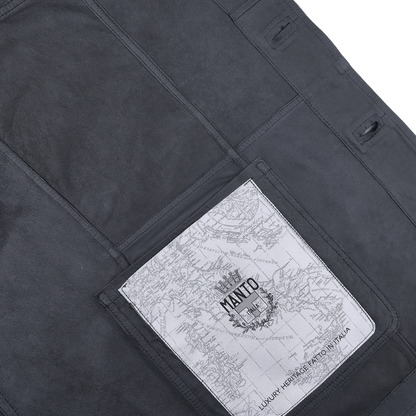 Close-up of a Denim Blue Suede Unlined Jacket by Manto, featuring a map printed on a white rectangular pocket. Text reads "Manto" with additional decorative elements, seamlessly blending rugged style and modern detail.