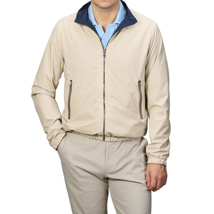 A person in Manto's Navy Beige Reversible Nylon Blouson, with coordinating pants and a blue shirt, stands with one hand in their pocket against a gray background. The sleek slim-fit design enhances the modern aesthetic.