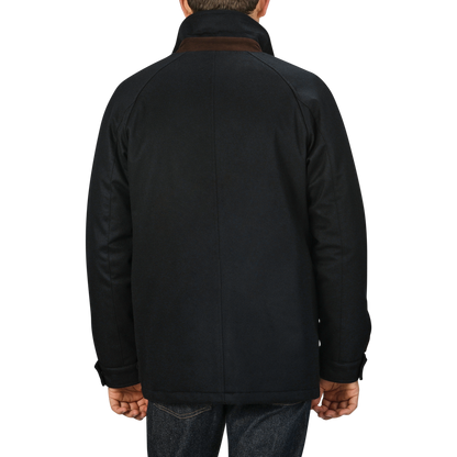 A person wearing a Navy Blue Cashmere Car Coat by Manto and jeans is standing with their back facing the camera against a plain gray background.