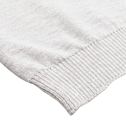 Close-up of the Cream Summer Mouline Crew Neck Sweater by Maurizio Baldassari, showcasing its white knitted fabric edge with ribbed detailing on a flat surface and highlighting the texture typical of a summer mouline knit.