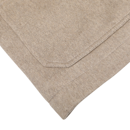 Close-up view of a beige folded fabric with visible stitching on a white surface, showcasing the texture and elegance of the Beige Cashmere Half Padded Chore Coat by Maurizio Baldassari.