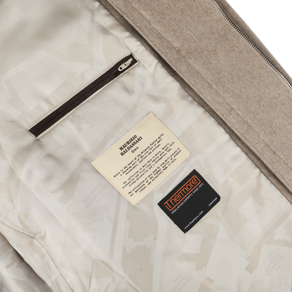 Close-up of a garment's interior revealing two labels sewn onto the fabric—one with care instructions and the other displaying the brand "Maurizio Baldassari." A zipper pocket is also partially visible, reminiscent of details you'd find in a high-end Beige Cashmere Half Padded Chore Coat.