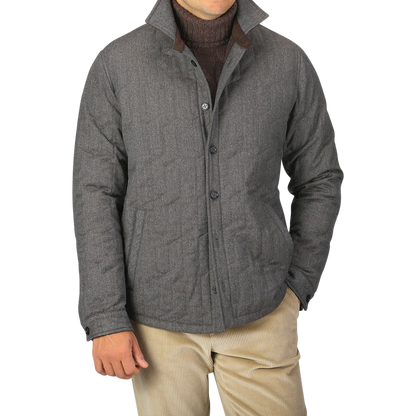A person wearing a Maurizio Baldassari Taupe Beige Herringbone Quilted Virgin Wool Overshirt over a dark sweater and light-colored pants, with their hands partially in their pockets.
