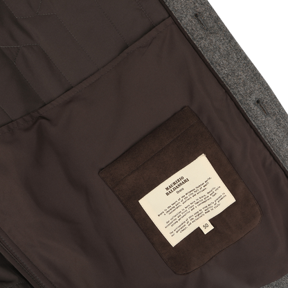 The image shows the inside of a Taupe Beige Herringbone Quilted Virgin Wool Overshirt by Maurizio Baldassari, featuring a brown interior made from virgin wool. A beige label with text is sewn onto a brown pocket on the left side.