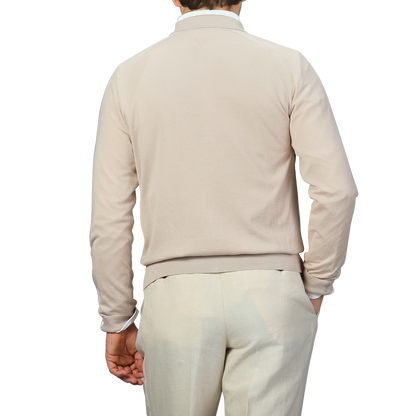 Against a plain background, a person embodies the subtle elegance of Italian knitwear while wearing Maurizio Baldassari's Beige Silk Cotton Full Zip Tennis Polo Shirt paired with light-colored pants, shown from the back.
