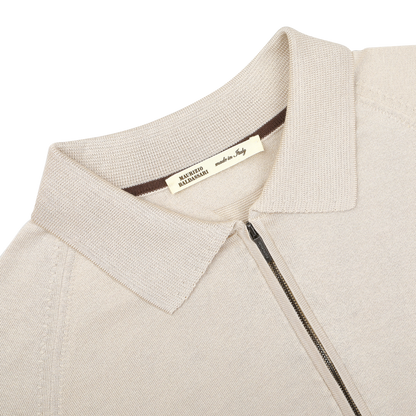 A close-up of the Beige Silk Cotton Full Zip Tennis Polo Shirt by Maurizio Baldassari highlights a textured collar and "Made in Italy" tag, showcasing exquisite Italian craftsmanship in luxurious silk-cotton knitwear.