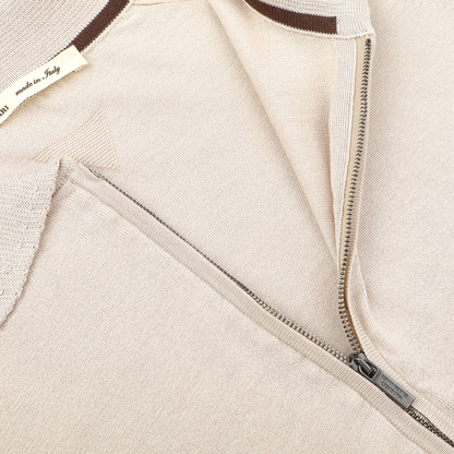 Close-up of a beige silk cotton full zip polo shirt by Maurizio Baldassari, partially open zipper shows a brown and white "made in Italy" tag. This exquisite piece embodies the essence of Italian knitwear, merging contemporary design with timeless elegance.
