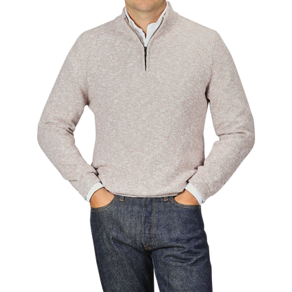 A person is wearing a Beige Winter Wool Mouline 1/4 Zip Sweater by Maurizio Baldassari and dark blue jeans, with their hands resting in their pockets. The background is a plain light gray color.