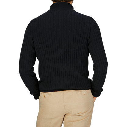 Man wearing a Black Cotton Silk Cable-Knit 1/4 Zip Sweater by Maurizio Baldassari and beige trousers, viewed from the back.