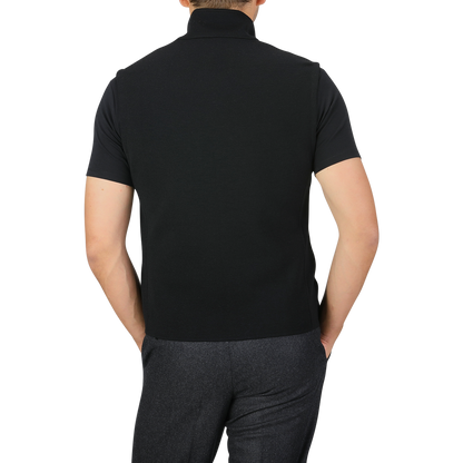 A person wearing the Maurizio Baldassari Black Milano Stitch Wool Zip Gilet and gray pants stands with their back to the camera, showcasing the intricate Milano stitch detail on their outfit.