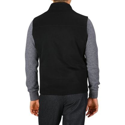 A rear view of a person wearing a Maurizio Baldassari Black Water Repellent Cashmere Gilet over a gray long-sleeve shirt and dark pants, standing against a white background.