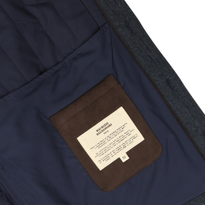 Close-up of the inside of a Blue Melange Quilted Virgin Wool Overshirt with a brown pocket. A white label with text is sewn onto the pocket. The overshirt, designed by Maurizio Baldassari, appears to be neatly lined and well-tailored.