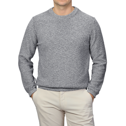 A person wearing a Blue Melange Summer Mouline Crew Neck Sweater by Maurizio Baldassari and beige pants stands with hands in pockets against a plain background.