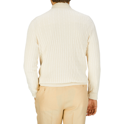 Rear view of a person wearing a Maurizio Baldassari cream cotton silk cable knit 1/4 zip sweater and light beige trousers.