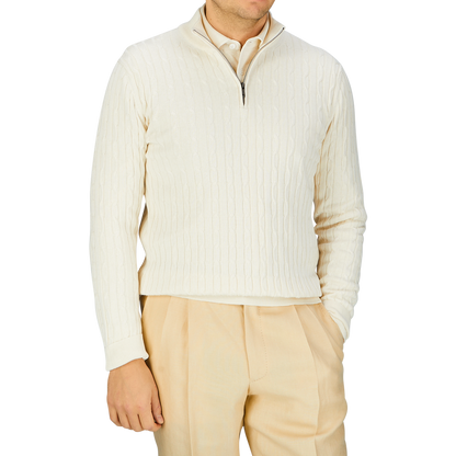 A person wearing a Cream Cotton Silk Cable Knit 1/4 Zip Sweater crafted by Maurizio Baldassari, with a zipper collar and light beige trousers.