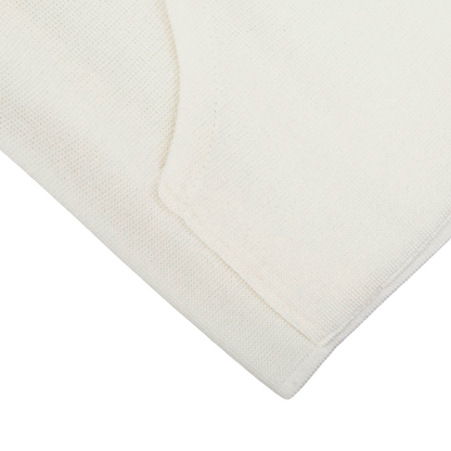 Close-up of a folded Cream Milano Stitch Wool Zip Gilet by Maurizio Baldassari, crafted from pure virgin wool, against a beige background.