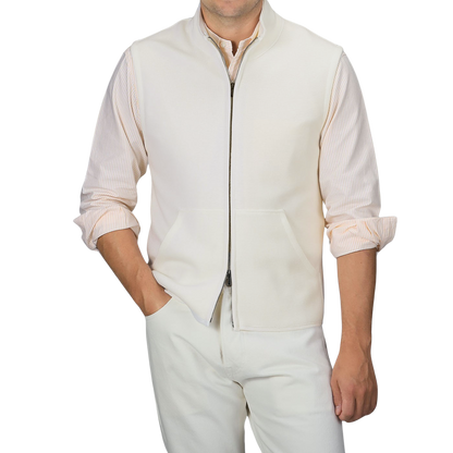 A person is wearing a Maurizio Baldassari Cream Milano Stitch Wool Zip Gilet over a striped shirt with rolled-up sleeves and light-colored pants. One hand is in the gilet pocket and the other by their side.