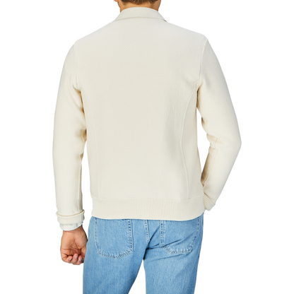 Rear view of a person wearing a Maurizio Baldassari Cream Beige Silk Cotton Knitted Blouson and blue jeans.