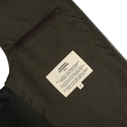 Close-up of a label on the inside of a Maurizio Baldassari Dark Green Water Repellent Cashmere Gilet, displaying care instructions for cashmere and a sizing label marked "50" on greenish-brown material, with a zipper and pocket visible.