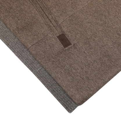 Close-up of a folded fabric with a visible seam, featuring a small brown tag and the luxurious feel of cashmere, showcasing the Dark Taupe Water Repellent Cashmere Gilet by Maurizio Baldassari.