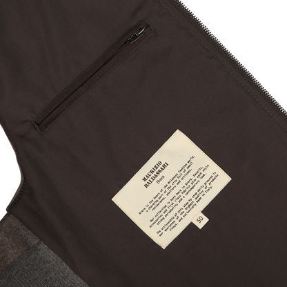 Close-up of the Dark Taupe Water Repellent Cashmere Gilet interior featuring a zippered pocket, a beige label with instructions and information, and crafted from luxurious cashmere by Maurizio Baldassari.