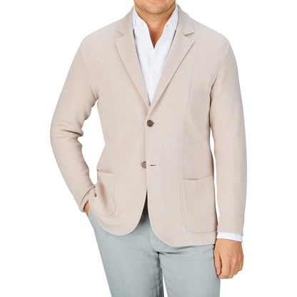 Man in a Maurizio Baldassari light beige silk cotton knitted Milano blazer and light grey pants with a white shirt unbuttoned at the collar, offering a casual substitute to formal wear.