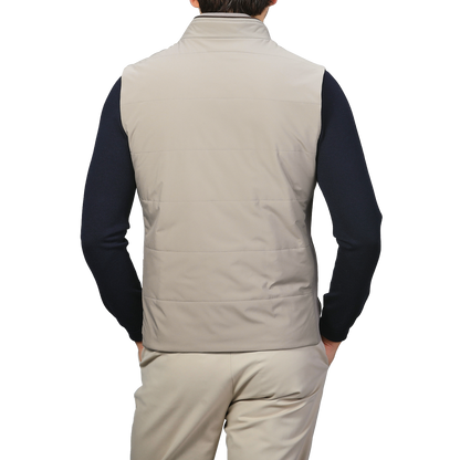 A person wearing a Maurizio Baldassari Pale Beige Nylon Thermore Travel Gilet, paired with beige pants and a navy long-sleeve shirt, seen from the back.