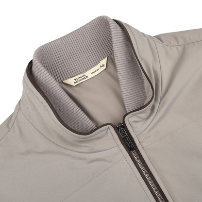 Close-up of a Pale Beige Nylon Thermore Travel Gilet by Maurizio Baldassari, featuring a ribbed collar and visible zipper. "Made in Italy" tag ensures lightweight comfort and style in this spring design.