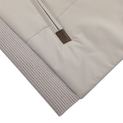 A close-up of the Pale Beige Nylon Thermore Travel Gilet by Maurizio Baldassari shows its smooth technical nylon material with a zipper featuring a brown leather tab. The gilet offers Thermore insulation and ribbed cuffs for added comfort.