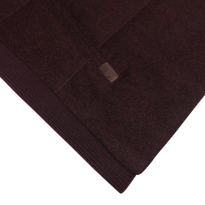 Close-up image of the Plum Water Repellent Cashmere Gilet by Maurizio Baldassari, showcasing a rich burgundy fabric with visible stitching and a small leather tag.