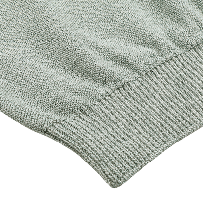 Close-up of the Maurizio Baldassari Sage Green Summer Mouline 1/4 Zip Sweater, highlighting its intricate knitted texture and ribbed hem against a simple backdrop.