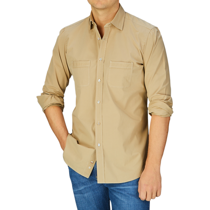 A man wearing a Khaki Beige Cotton Gabardine Regular Fit Shirt by Italian shirtmaker Mazzarelli and stone-washed blue jeans against a blue background.