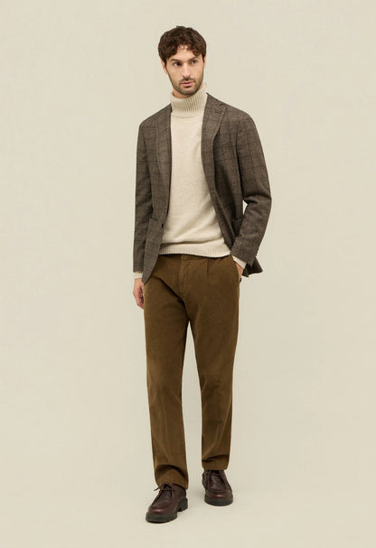 Man wearing a brown blazer, beige sweater, and brown pants on a beige background