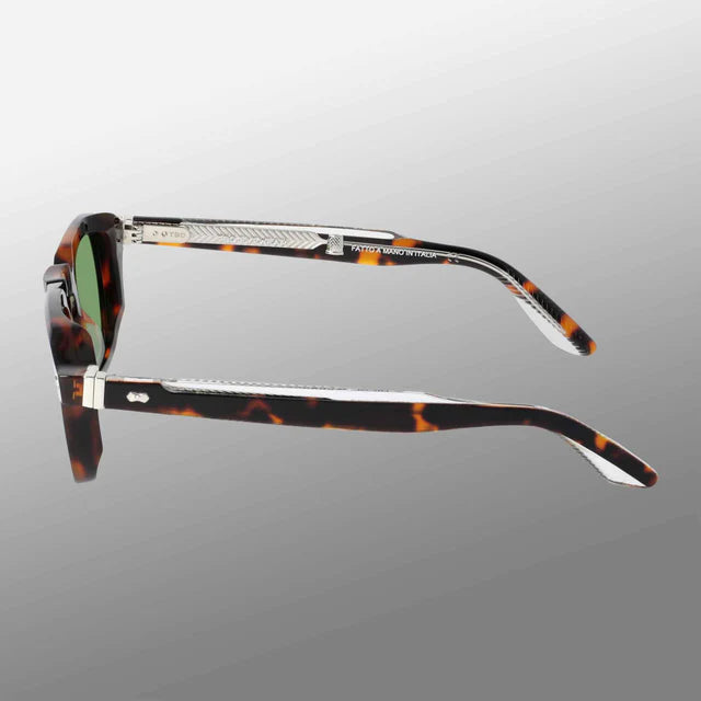 Side view of Ply Brown Havana | Green sunglasses by TBD Eyewear, showcasing rectangular lenses in a brown and amber acetate renew frame with silver accents and small text on thick arms. Background fades from light to dark gray. , available at Richard Gelding Mayfair