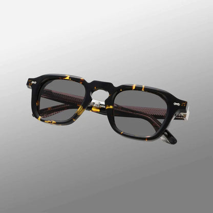 The Ply Black Havana | Grey sunglasses by TBD Eyewear are thick, rectangular frames handcrafted in Italy, with a black and yellow tortoiseshell acetate renew pattern and transparent temples, angled on a smooth gray gradient background. , available at Richard Gelding Mayfair
