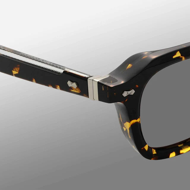 Close-up of Ply Black Havana | Grey eyeglasses by TBD Eyewear, handcrafted in Italy with a glossy black and yellow tortoiseshell pattern. The metal hinge joins the frame front and arm, set against a clean light gray gradient background. , available at Richard Gelding Mayfair