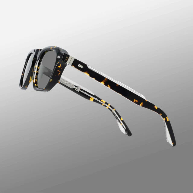 The Ply Black Havana | Grey sunglasses by TBD Eyewear are handcrafted in Italy with thick, premium acetate renew frames, dark grey-tinted lenses, and arms showcasing a mottled amber and black pattern with metallic accents. , available at Richard Gelding Mayfair