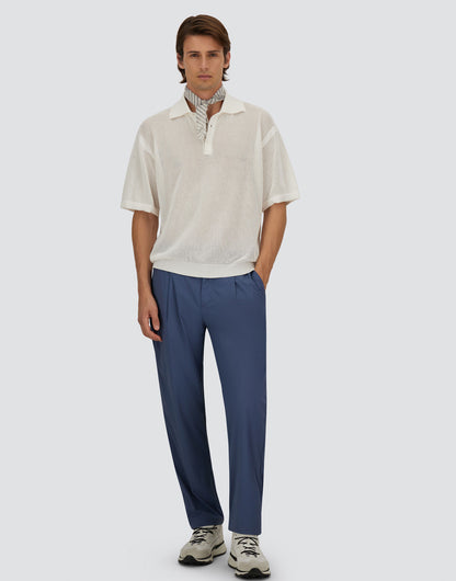 A man with medium-length brown hair and a neutral expression wears Herno Blue Lightweight Nylon Drawstring Casual Trousers, a sheer white polo layered over a striped collared top, and white sneakers against a plain light gray background. , available at Richard Gelding Mayfair