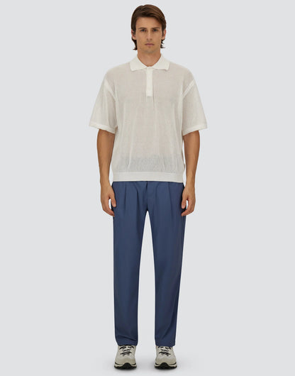 A man with medium-length dark hair combed back stands against a plain light gray background, wearing a sheer white short-sleeve polo over a white undershirt, white sneakers, and Herno Blue Lightweight Nylon Drawstring Casual Trousers. , available at Richard Gelding Mayfair