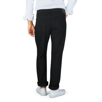 Person wearing black Paige Black Shadow Cotton Transcend Normandie Jeans in a regular fit and white shoes standing against a neutral background.