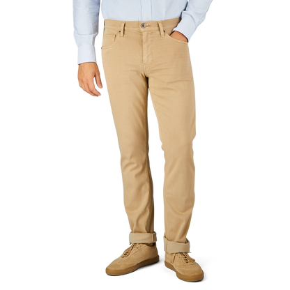 A person wearing a light blue shirt, Caramel Beige Cotton Transcend Federal Slim Jeans from Paige rolled up slightly at the bottom for a comfortable fit, and beige shoes stands against a plain background.