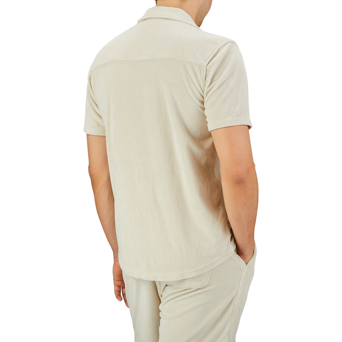 A person wearing a Paige Cream Beige Cotton Towelling Polo Shirt and matching shorts stands with their back to the camera, one hand casually tucked in their pocket.