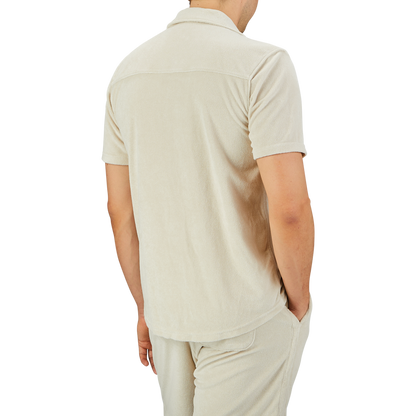 A person wearing a Paige Cream Beige Cotton Towelling Polo Shirt and matching shorts stands with their back to the camera, one hand casually tucked in their pocket.