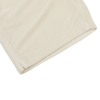 A close-up view of a beige-colored, folded pair of Cream Beige Cotton Towelling Shorts by Paige, made from a towelling cotton blend, on a white surface.