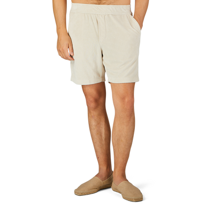 A person wearing Paige's Cream Beige Cotton Towelling Shorts with a drawstring waist and beige slip-on shoes is standing against a plain background with one hand in their pocket.