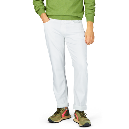 Man in green sweater and Paige Icecap White Cotton Transcend Federal Slim Jeans standing with one hand in pocket, wearing multicolored sneakers.